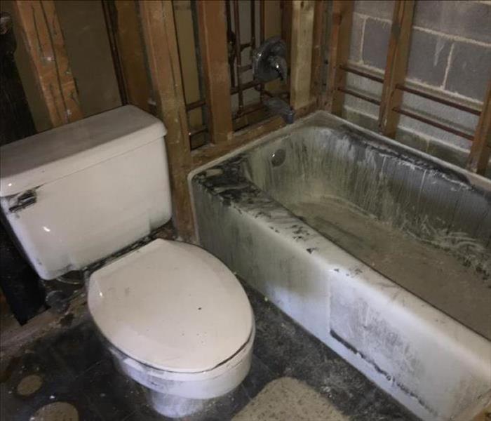 Soot covered bathtub and toilet in a bathroom.