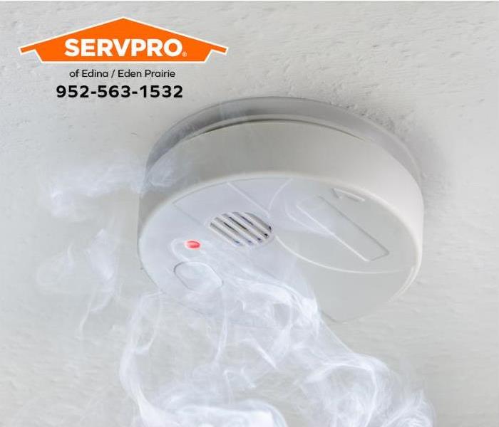 White smoke alarm with smoke on a white ceiling.