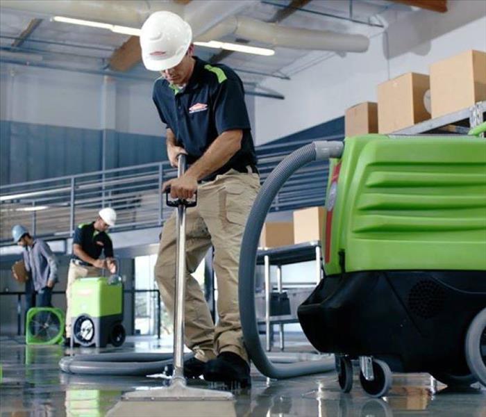 SERVPRO employee with a white hard hat using a green water extractor in a warehouse.